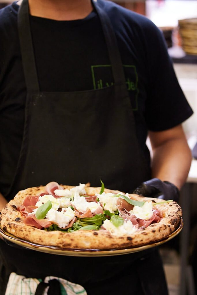 Chef holding a wood-fired prosciutto pizza at Il Verde Italian restaurant in Bowen Hills Brisbane
