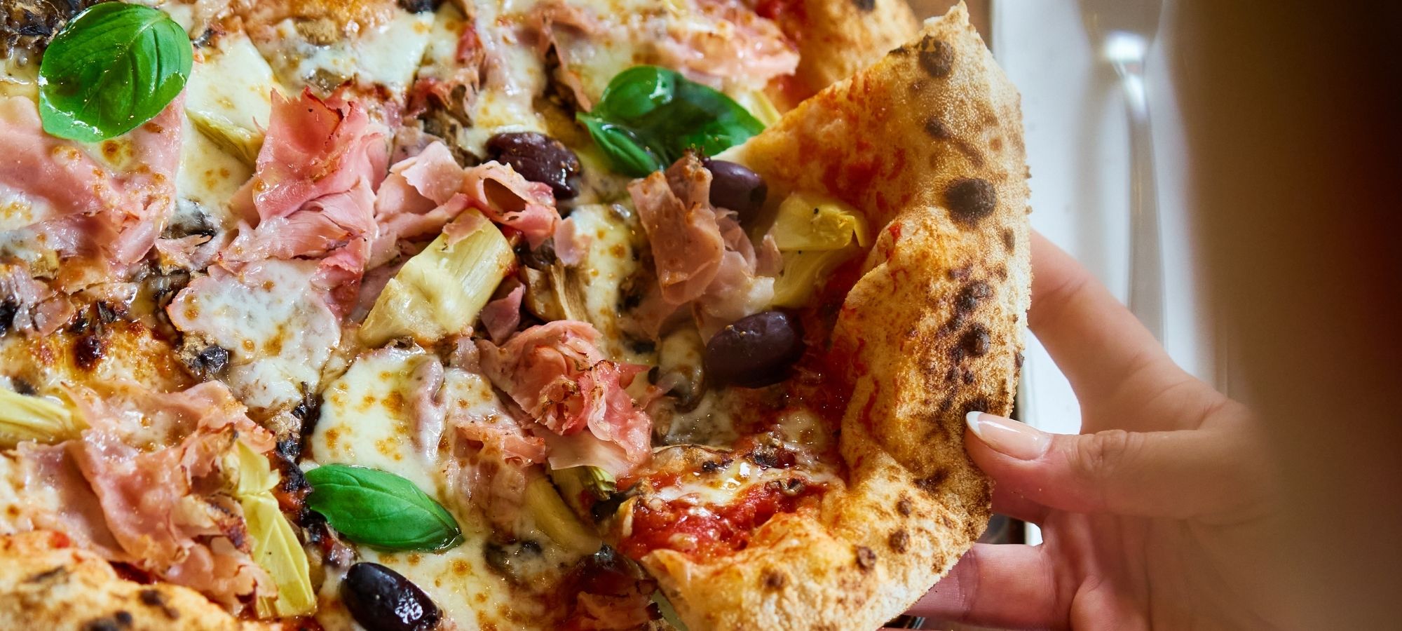 Hand holding a slice of wood-fired prosciutto pizza at Il Verde Italian restaurant in Bowen Hills Brisbane